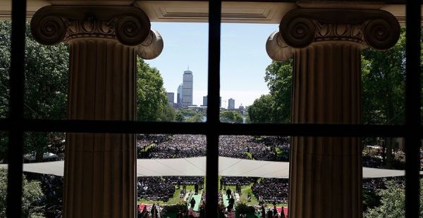 Pillars of Killian court frame a view of the commencement ceremony with the Boston skyline in the background