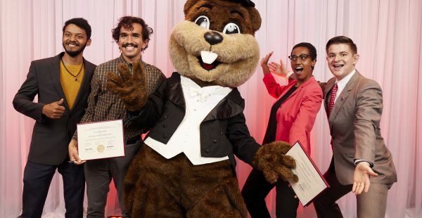 Group of four alumni posing with Tim the Beaver MIT Mascot and holding awards