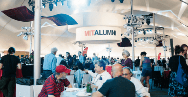 Large group of alumni sitting under a white tent with a hanging MIT Alumni banner.