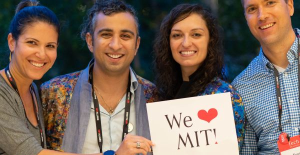 Chest up shot of four people (two women, two men) smiling and holding a sign that says "We [heart] MIT!"
