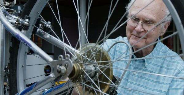 Neal Carlson is shown through the spokes of a bicycle. He is looking at the gears.