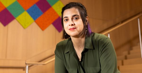 Portrait of Michelle Spektor PhD ’23 from waist up. A stairway railing is visible behind her as is a wooden wall with artwork made of blocks of color.