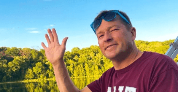 Headshot of Andy Obst ’90 waving while on a boat, sunglasses perched on his head. He's wearing an MIT t-shirt