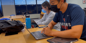 Two MIT students with masks on looking at their laptops 
